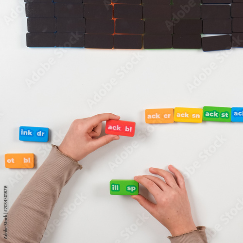 Fotografía Top view of child's hands arranging colorful phonics word domino tiles on a white background