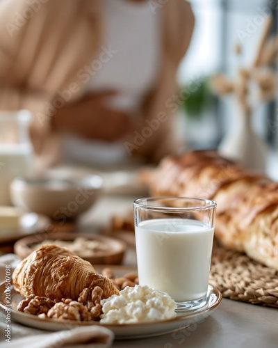Glass of milk with croissant and bakery products on breakfast table, person holding stomach in background, concept of gluten intolerance and digestive sensitivity