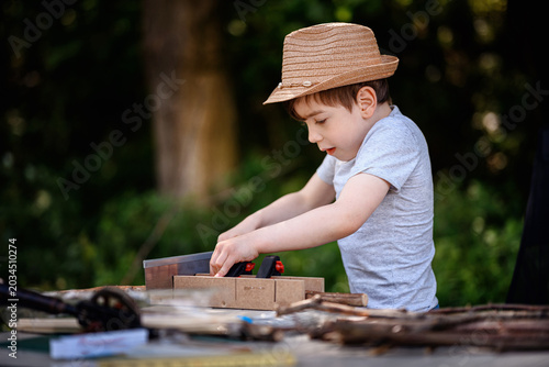 Little boy working outdoors cutting wood with saw on camping table