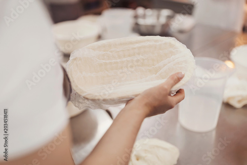Baker prepares sourdough dough in basket at bakery for leavening and cooking in workshop setting
