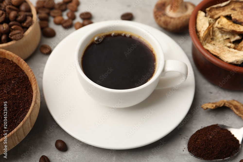 Obraz premium Cup of coffee, beans, powder and mushrooms on light grey table, closeup