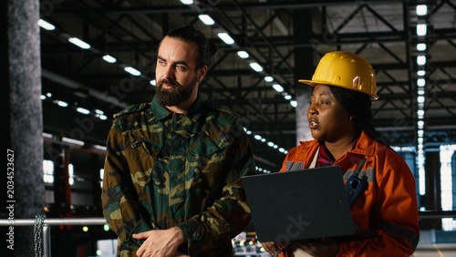 Photos Military officer and engineer discussing armament production in heavy industry warehouse, war effort and mobilization for national defense, Wartime industry with diverse people