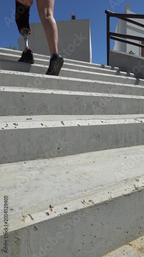 Low-angle view of an athletic woman with a prosthetic leg walking up a concrete staircase. She shows resilience and determination overcoming adversity