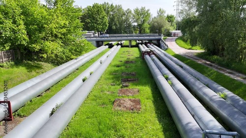 Aerial view of industrial pipes for gas, water, and oil running parallel across a green landscape, showcasing their weathered surfaces and surrounding vegetation in a natural setting