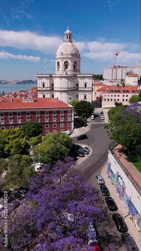 Lisbon, Portugal - May 25, 2026: Establishing shot of purple jacaranda trees in bloom at Jardim Botto Machado, Campo de Santa Clara, Lisbon, with historic architecture.