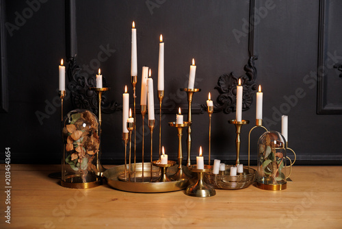 Cuadro en lienzo Brass candlesticks and lit taper candles arranged with glass cloches containing dried flowers on a wooden tabletop, creating a warm, moody, elegant still life and cozy interior atmosphere