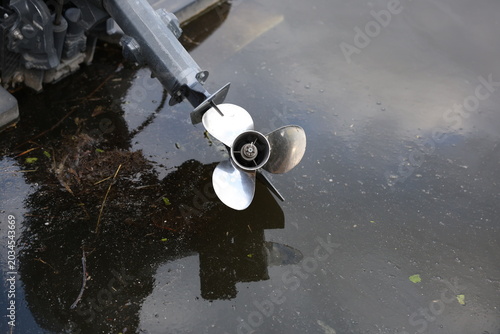 Canvastavla Close-up view of a stainless steel outboard propeller partially submerged above murky water, showing blades, motor housing and reflection
