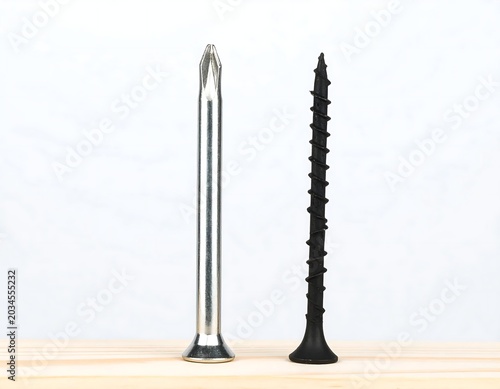 Metal Nail and Black Screw Standing Upright on Wooden Surface
