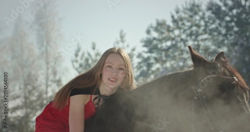 Woman in red dress hugging horse in winter forest