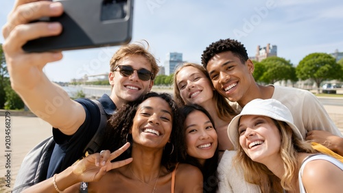 A group of diverse young adults taking a selfie together outdoors on a sunny day