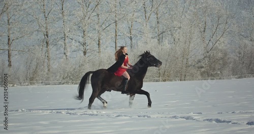 Beautiful woman in red dress riding horse in winter