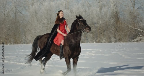 Young woman riding a black horse in a snowy field