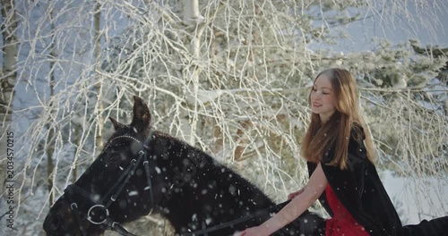 Beautiful young woman riding black horse in winter forest