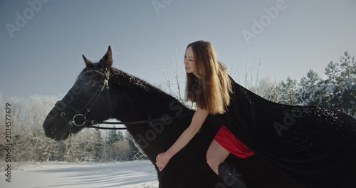 Beautiful woman in red dress riding black horse in winter