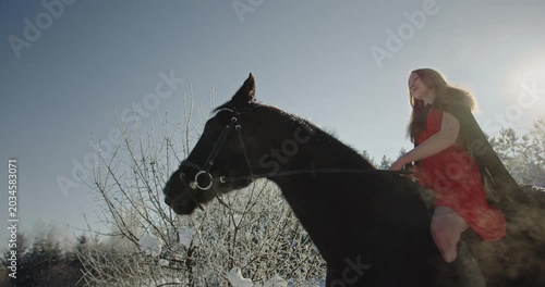 Young woman in red dress riding horse in winter forest