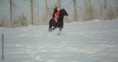 Beautiful woman riding black horse galloping through snow
