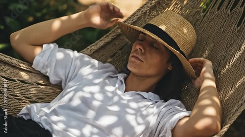 Young man relaxing in a hammock with a straw hat over his face for a digital detox and slow living