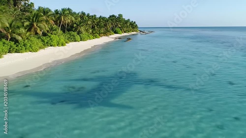 Aerial drone tracking over pristine tropical island, white sand beach, turquoise ocean, palms, jungle. Airplane shadow on water, golden light. Concept of luxury and serene arrival