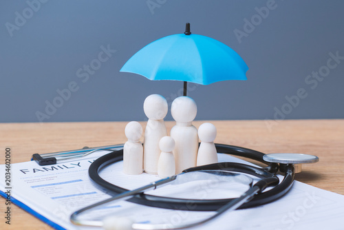 Obraz na plátně Family insurance concept with wooden figures with blue umbrella and stethoscope on policy form