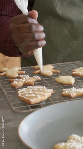 Vertical video: Positioning tip, hand icing cookies on rack at counter with piping bag, olive apron