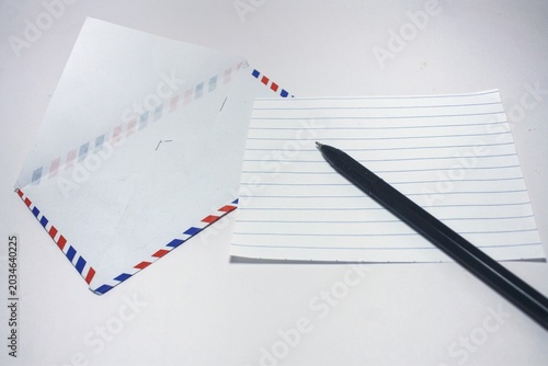 фотографія A black ballpoint pen resting on a blank lined paper next to an open airmail env