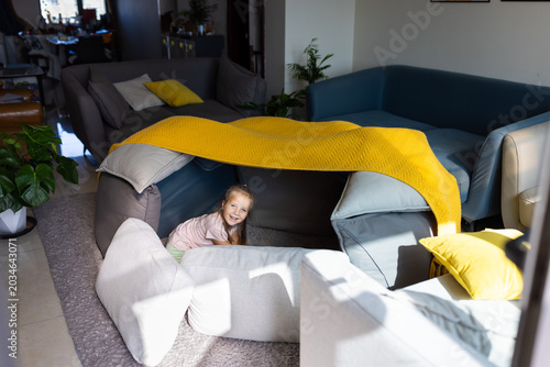 Smiling girl playing inside a sofa cushion fort in a cozy living room