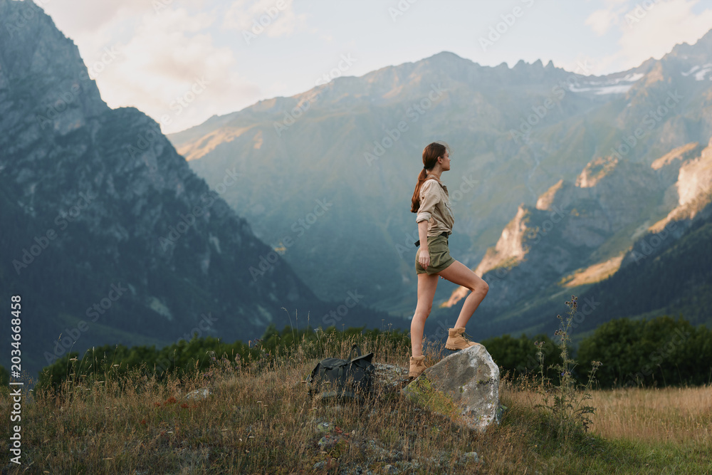 Naklejka premium Woman hiking outdoors, standing on a rock in a sunlit valley, embracing nature, casual outfit, confident pose, scenic mountains, peaceful atmosphere