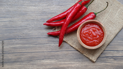 Chilli sauce and fresh peppers on wooden background