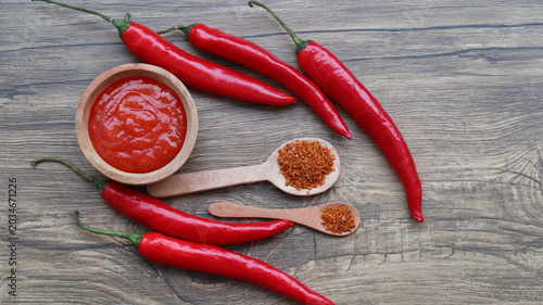 Canvas Print Chilli sauce, chilli flakes and fresh peppers on wooden background