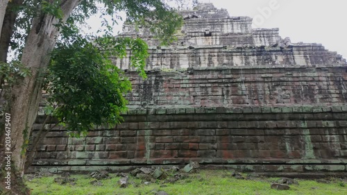 Ancient stone ruins of Koh Ker Pyramid Temple overgrown with moss and trees in Cambodia. The weathered stone blocks show signs of age and the encroaching jungle.