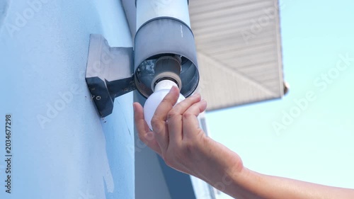 Close up shot of a person hand replacing or installing an energy-saving LED light bulb into an outdoor wall lamp fixture of a residential building