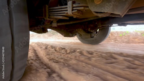 Low angle close up of a car tire driving on a dusty gravel road in rural countryside, capturing texture, motion and rugged travel atmosphere for road trip and transportation concepts