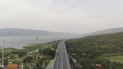 Aerial view of highway running along river and green hills. Transportation, infrastructure, travel and logistics concept