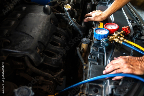Mechanic checking and refilling car air conditioning system with manifold gauge set in auto repair shop. Vehicle maintenance concept.