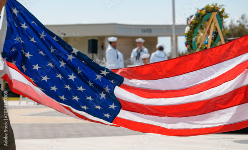 A large American flag is held during a ceremonial folding presentation at a memorial observance