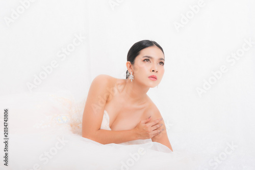 Portrait capturing an intimate moment with a beautiful Asian bride in a white gown, lying down gracefully with her hands clasped studio shot on white background.