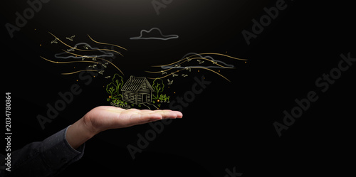 Tableau sur toile Hand holding glowing rural home drawing with trees, birds and dark copy space