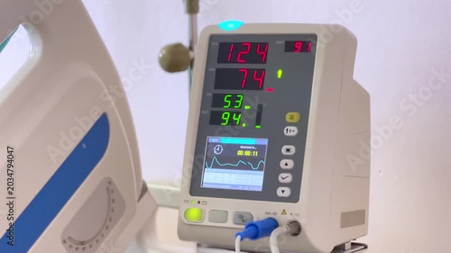 Patient monitor displaying vital signs including heart rate blood pressure oxygen saturation waveform hospital room medical equipment background care