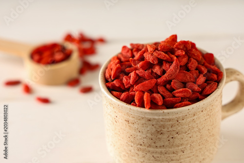 Fotografía Mug with dried goji berries on white wooden background, closeup