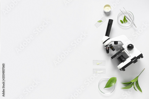 Modern microscope with different leaves, petri dish, mortar and pestle on whi...