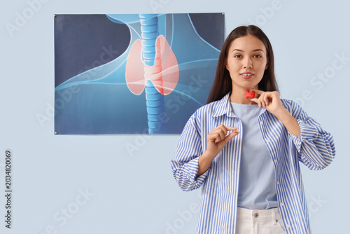 Young Asian woman with thyroid gland model and pill near picture on blue back...