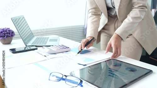 Business professional reviewing financial reports and performance charts at a modern office desk, analyzing data, planning strategy, and managing corporate documentation.