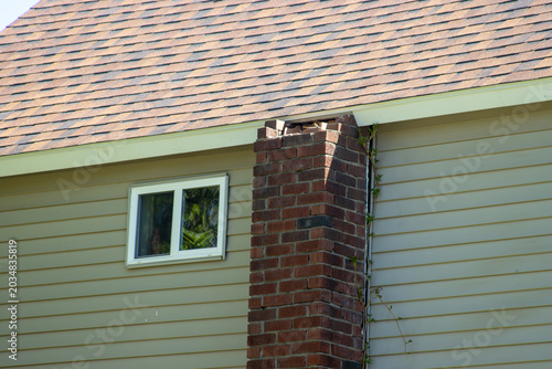 Bild auf Leinwand A brick chimney in need of repair on the side of a two-story wooden house