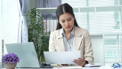 Young businesswoman reviewing financial documents and reports at a modern office desk, analyzing data and managing paperwork with focus and professionalism.