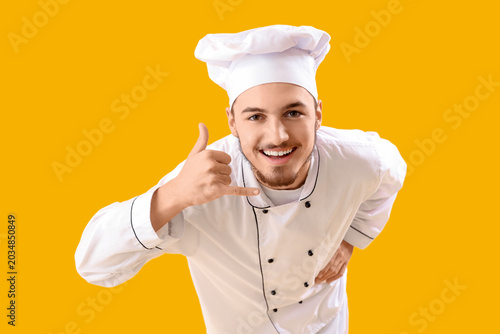 Fotografía Male chef showing call me gesture on yellow background