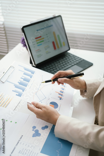 Business professional reviewing financial reports and performance charts at a modern office desk, analyzing data, planning strategy, and managing corporate documentation.