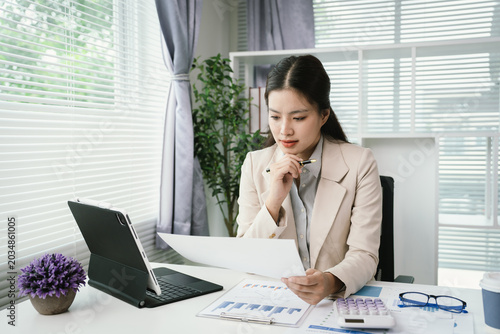 Young businesswoman reviewing financial documents and reports at a modern office desk, analyzing data and managing paperwork with focus and professionalism.