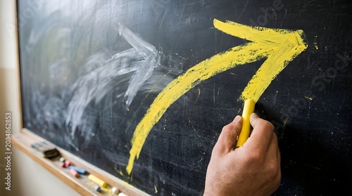 Hand a large yellow chalk arrow on a black chalkboard, showing growth, direction, and upward movement concept