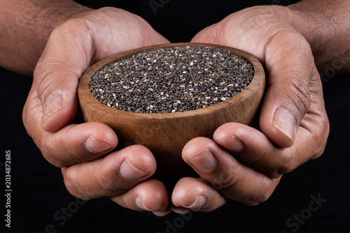 Hands holding a rustic wooden bowl of raw organic chia seeds against a simple background