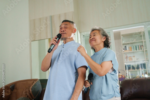 Happy Asian senior couple singing karaoke together at home, enjoying music, entertainment and quality time during retirement.
